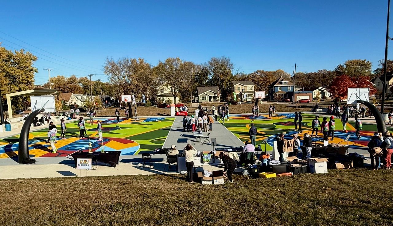 People gathering at a colorful, outdoor basketball court with various tables and activities.